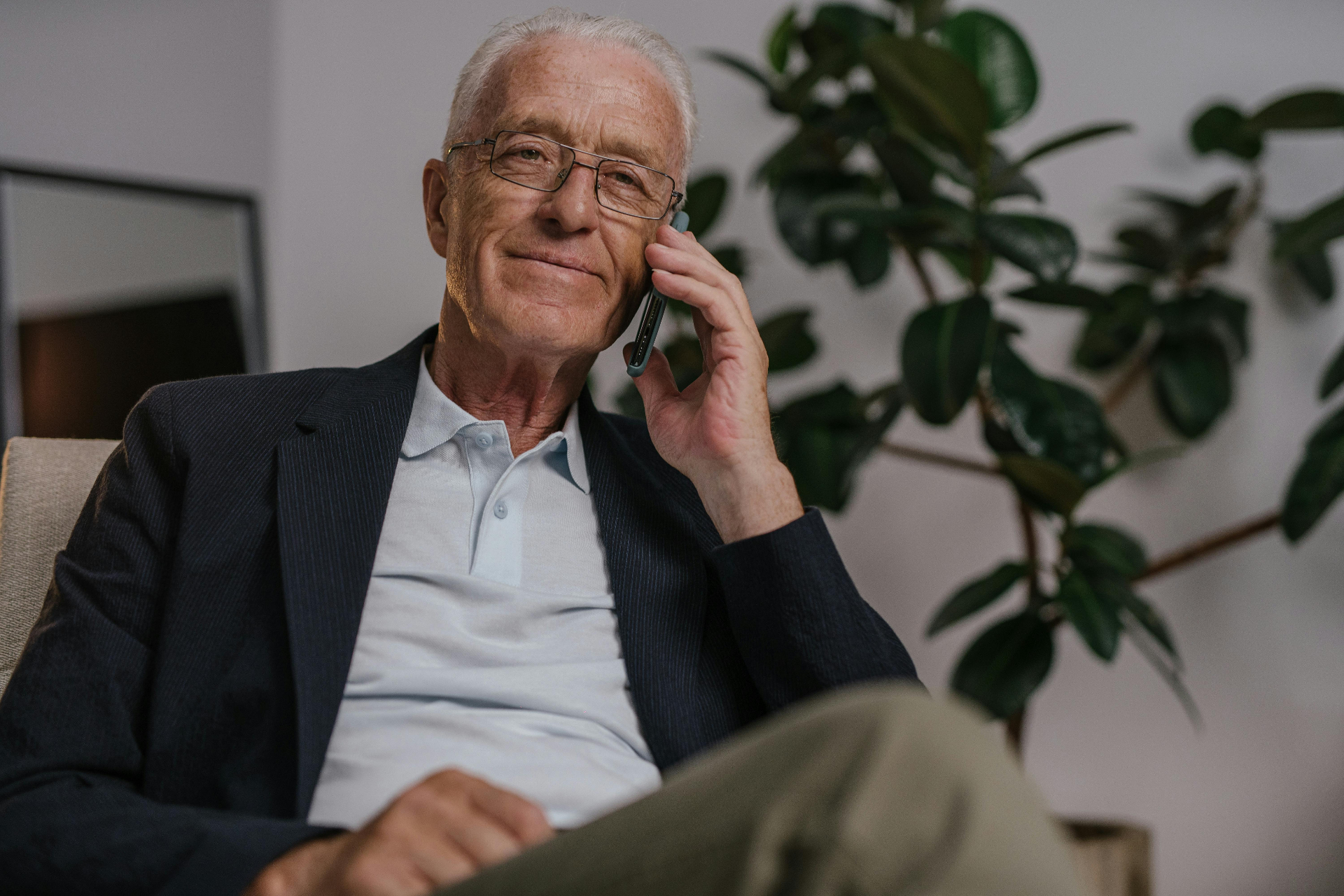 An older man smiling softly while talking on the phone at home